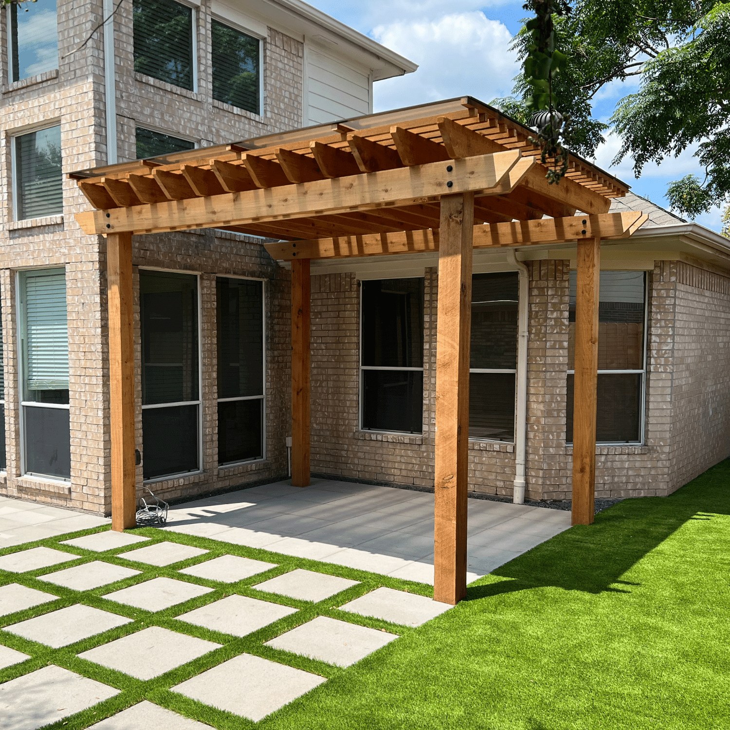 Spaced square patio pavers with grass joints beneath a wooden arbor
