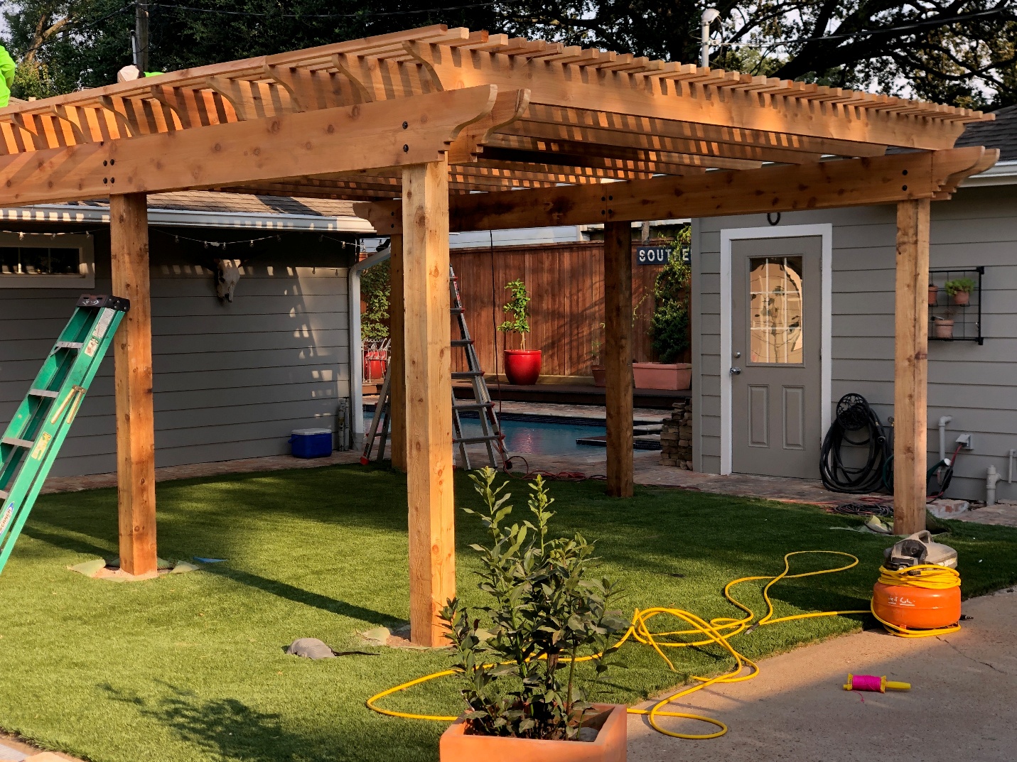 Wooden arbor with open roof slats during installation beside a home