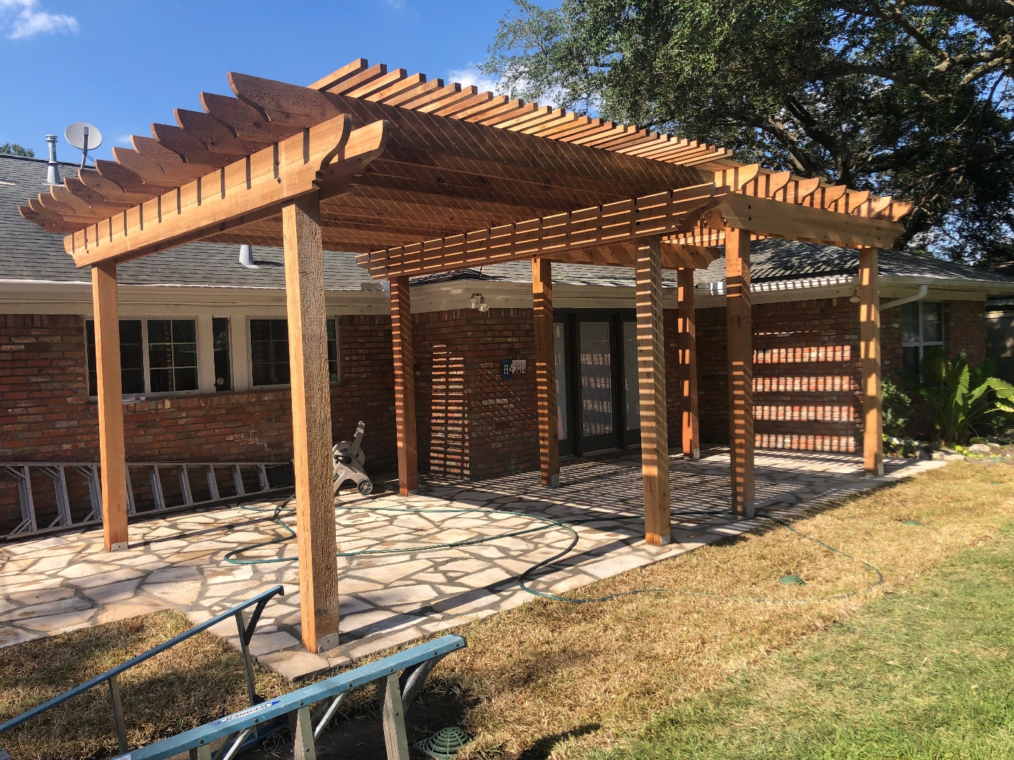 Wooden arbor with an open slatted roof over a garden patio